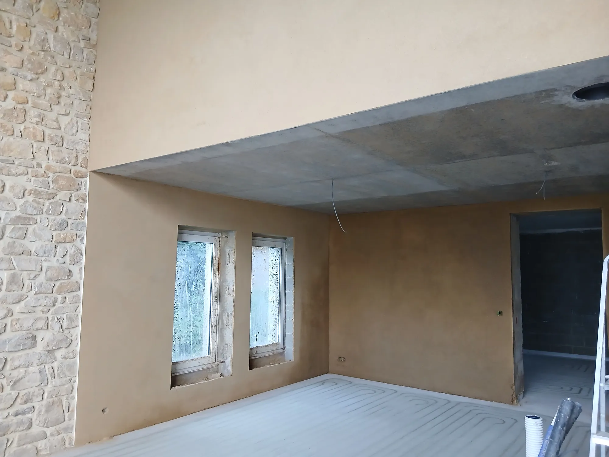 Séjour d'une maison en pierre enduit à l'argile, grande baie vitrée et plafond clair