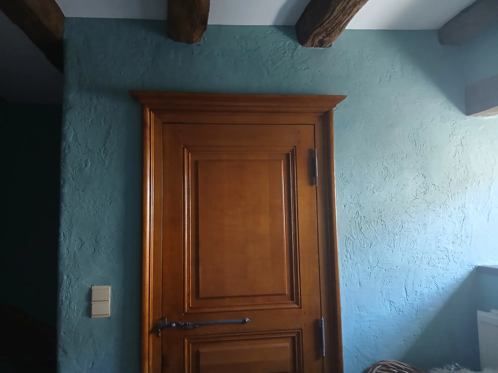 Pièce à poutres apparentes peinte en bleu canard mat avec porte en chêne